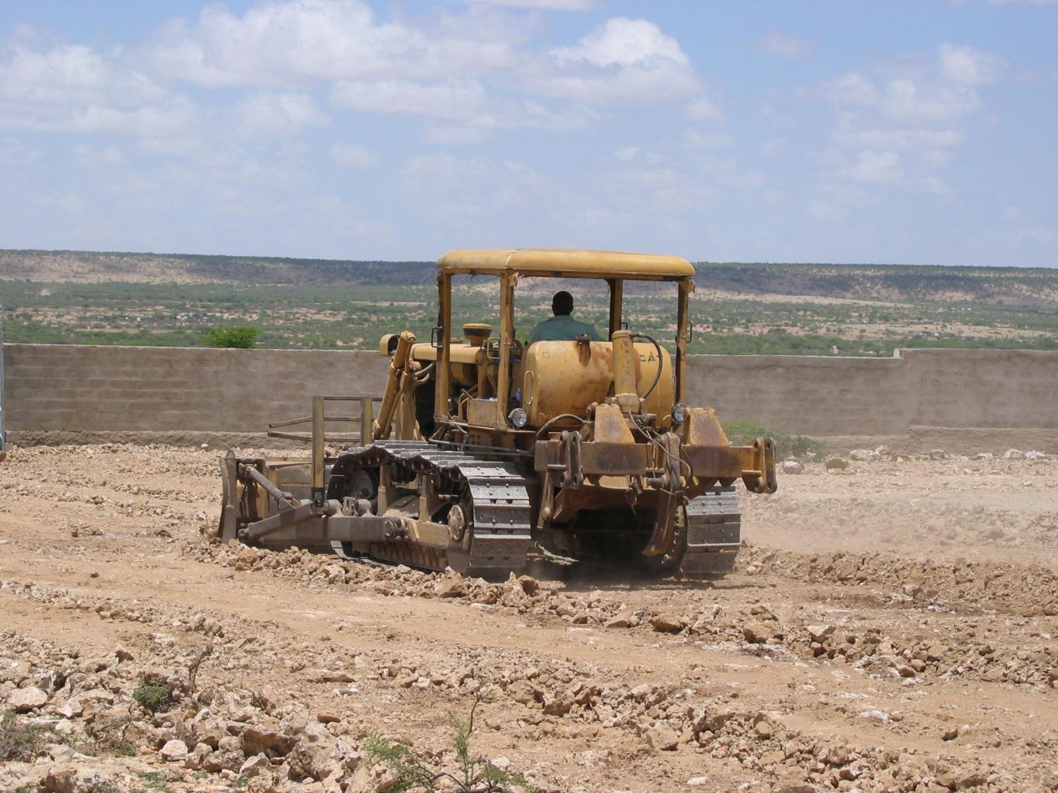 View of a bulldozer preparing to terrain. Perimeter wall in the background.