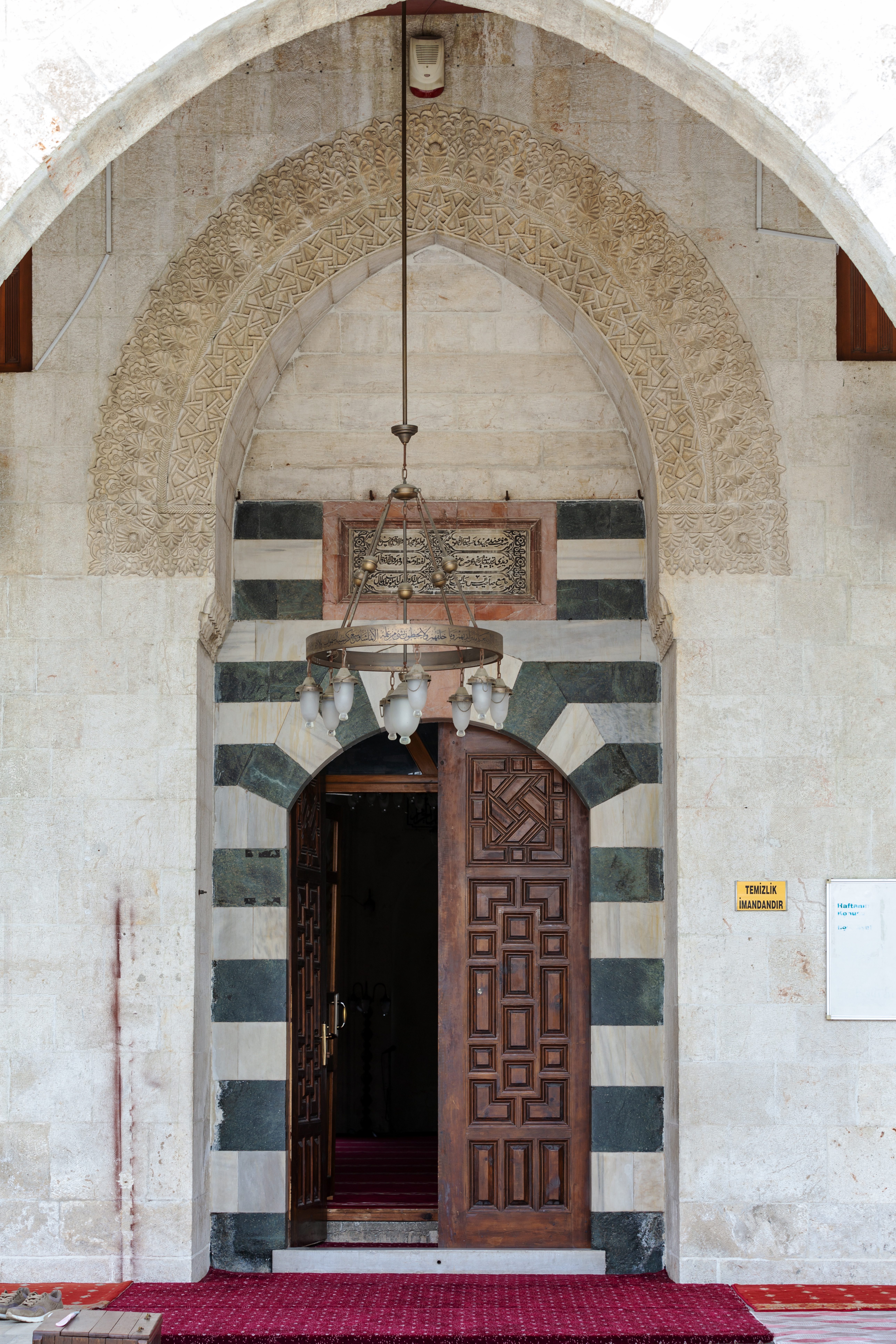 <p>View of the entrance with chandelier, inscription and carved wood door</p>