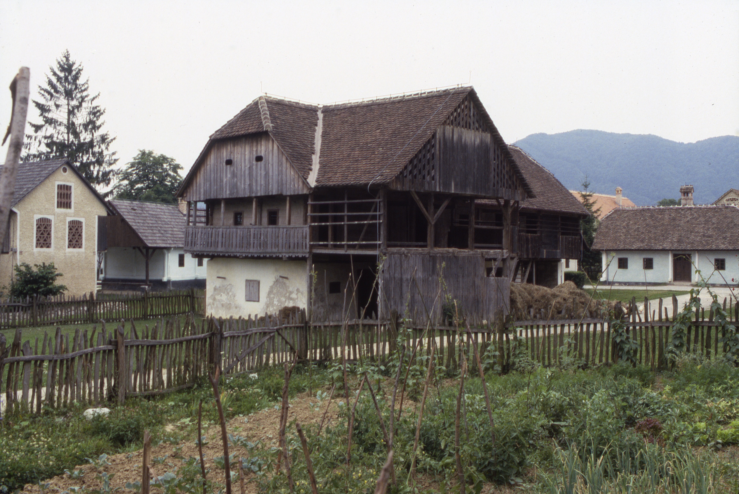 <p>A view of the large barn from another angle emphasizes its varied spaces, including projecting porch and upper-level gallery along the end of the main, gabled structure with the pent-hip at the top.</p>