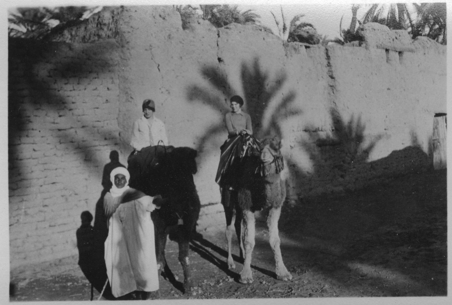 Women on camels outside earthen walls