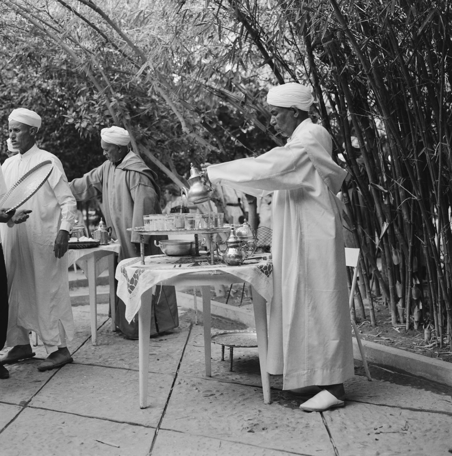 Men in traditional Moroccan clothing preparing and seving tea in a bamboo grove