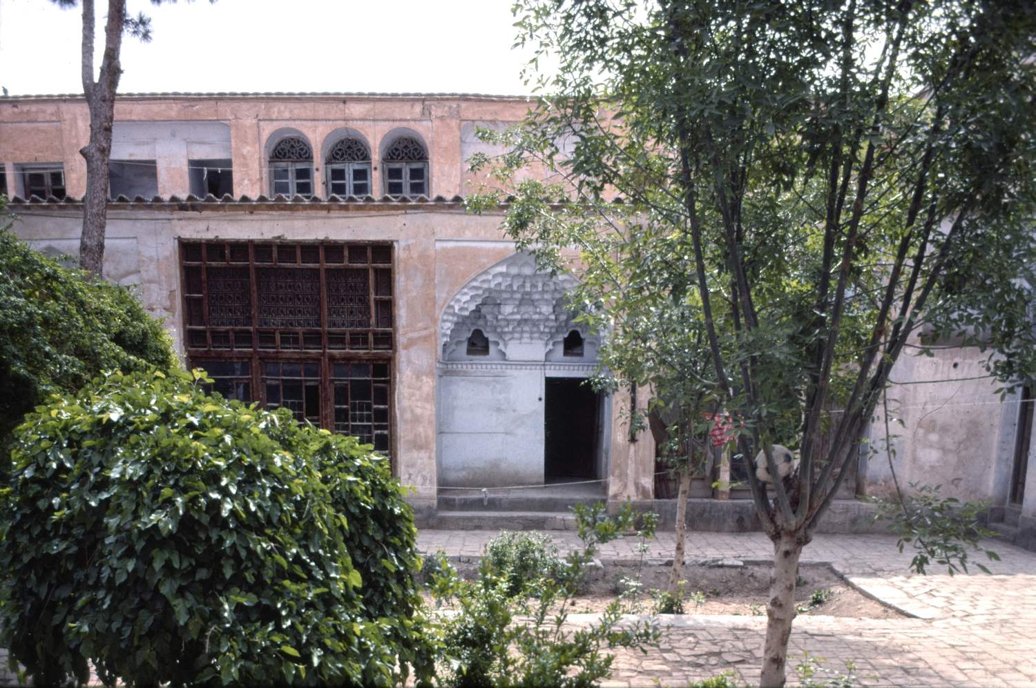 View of eastern facade of courtyard from west side, showing set of three wood-framed windows and muqarnas-vaulted recessed entryway.
