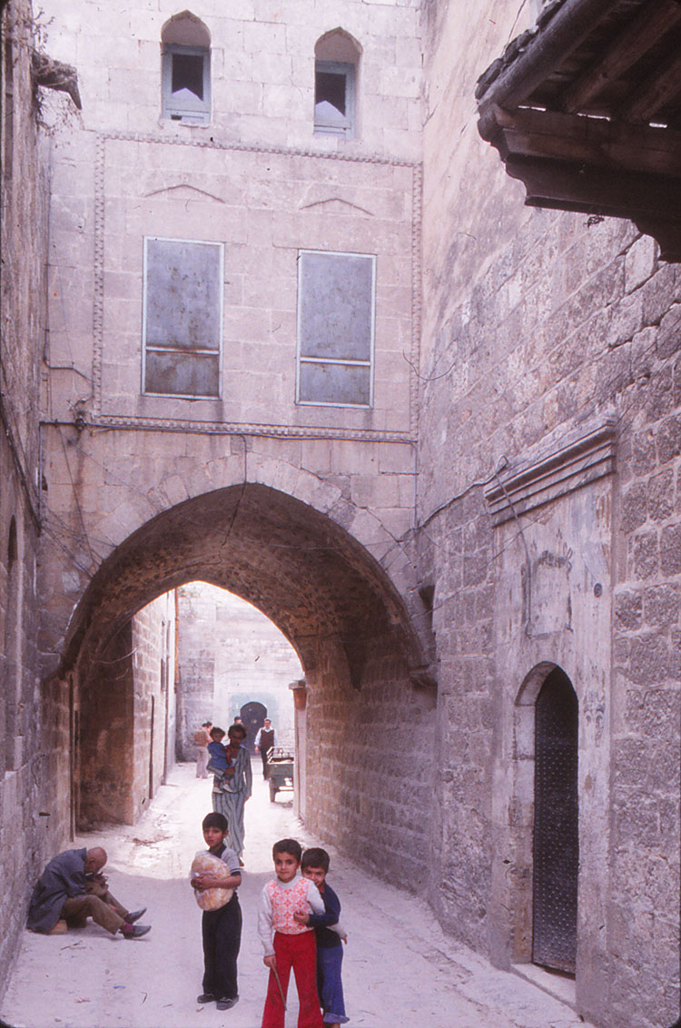 <p>Street passing under an arched elevated bridge connecting two buildings in the Bab Qinnasrin Quarter, Aleppo</p>