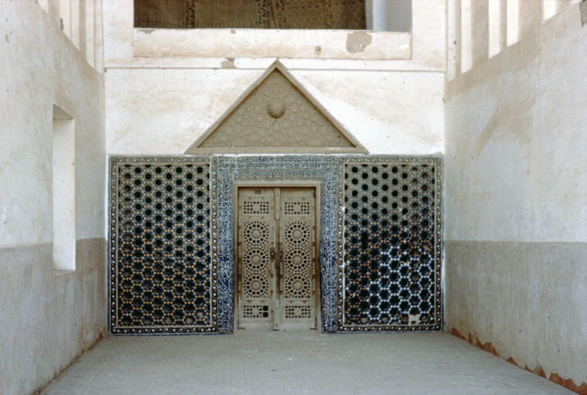 View of northeast entrance showing latticed wooden door framed by mosaic inscription band flanked by tile panels with triangular stucco panel above