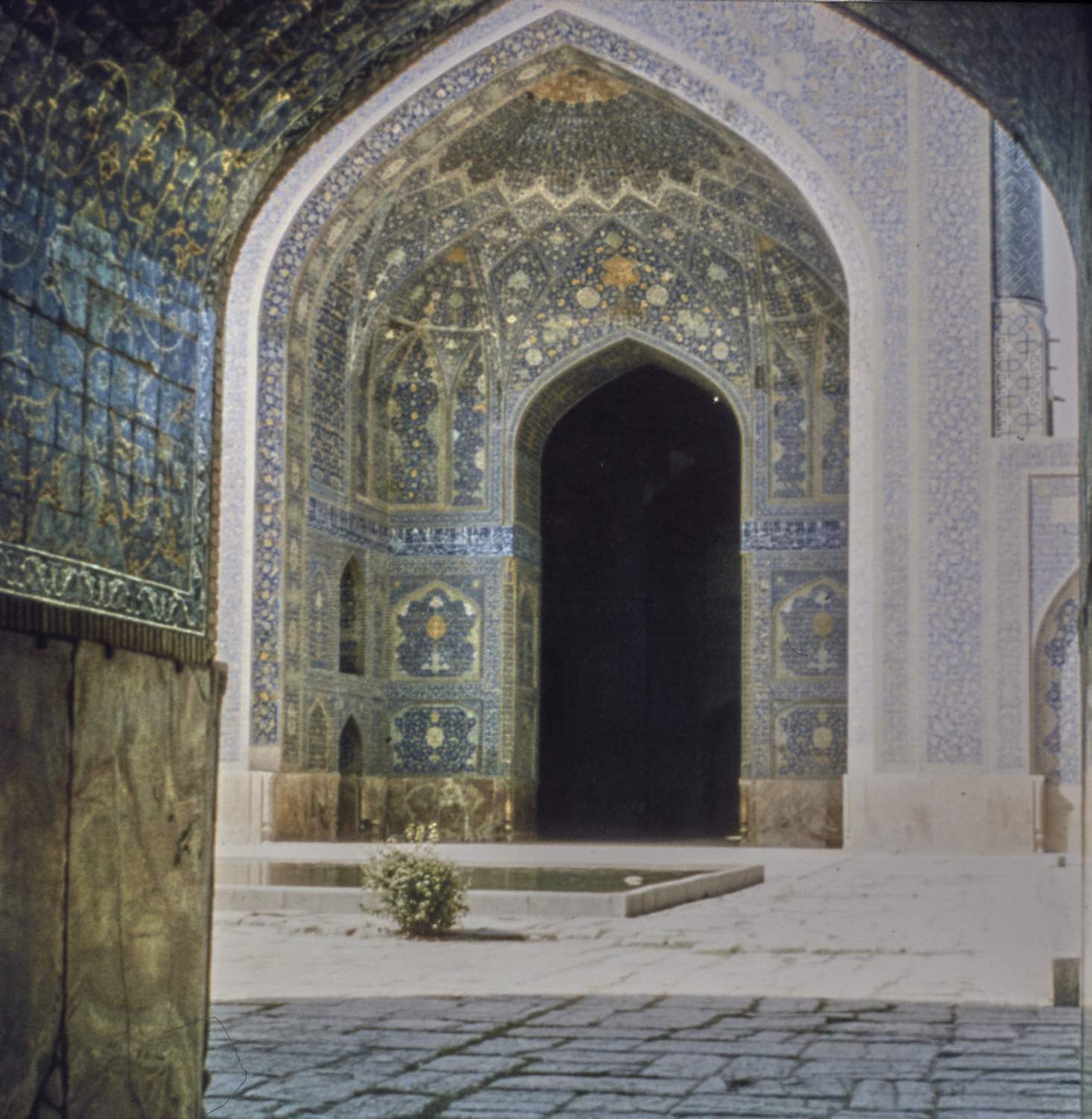View of entrance to qibla iwan from under an arch across courtyard.