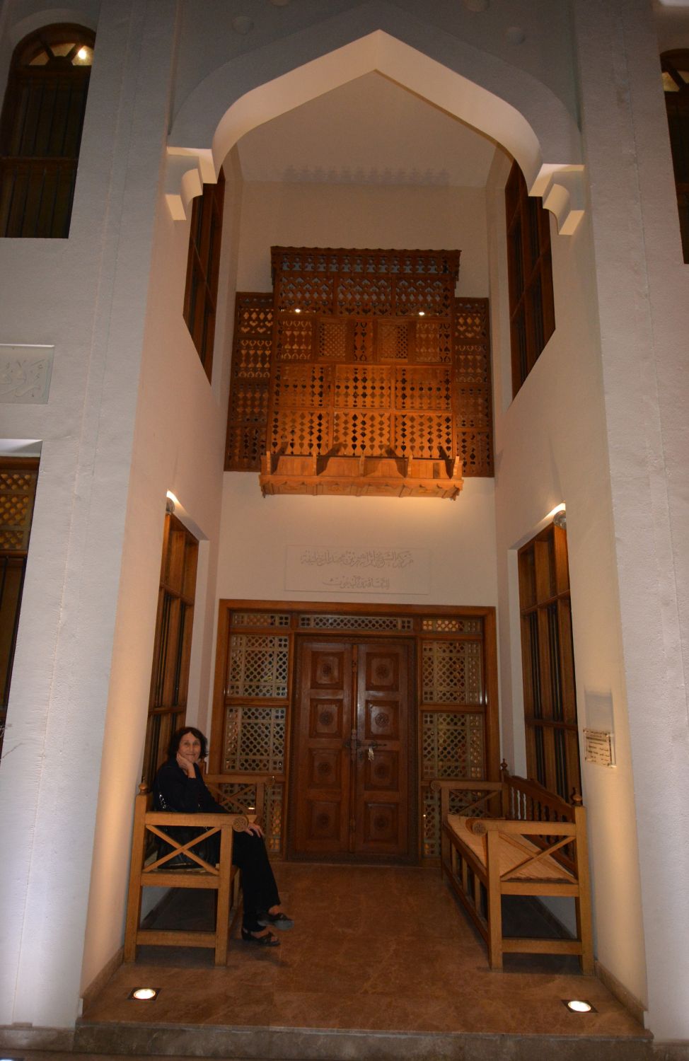 View of an iwan with a seated woman and ornate wood screens.