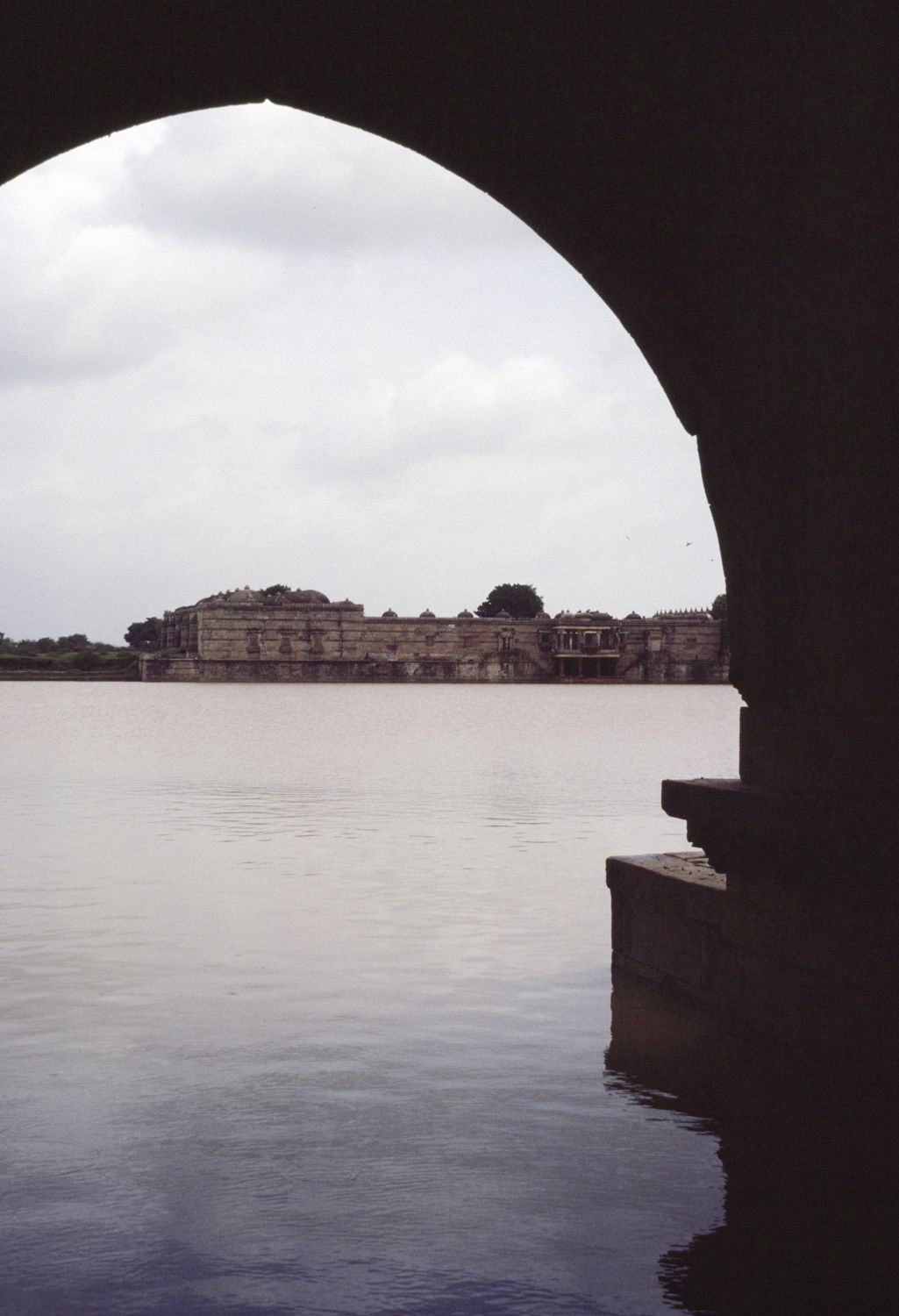View through archway of Mahmud Shah's Palace on the south bank of the tank, facing north across water. The southern facade of the mosque and tombs is visible in background.&nbsp;