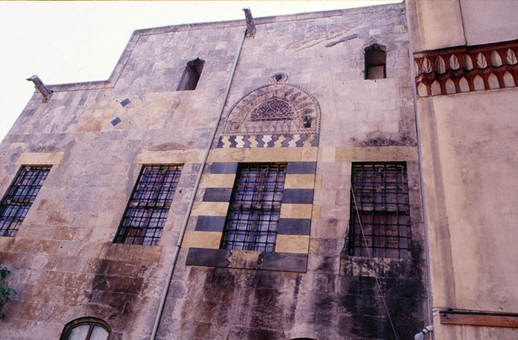 <p>Courtyard: view of southern end of east facade, showing ornate windows with ablaq decoration and lunette</p>