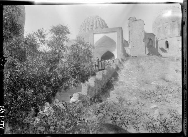 View from the southeast toward the middle chahar taq. The ribbed dome in the midground to the left belongs to the Amir Zadeh mausoleum. The domed structure to the right is the Shirin Beg Agha mausoleum, before which stand the ruins of the Amir Husayn ibn Tughluq Tekin mausoleum. One of the domes of the anonymous mausoleum III ("Qazizadeh Rumi") is partially visible behind the foreground foliage