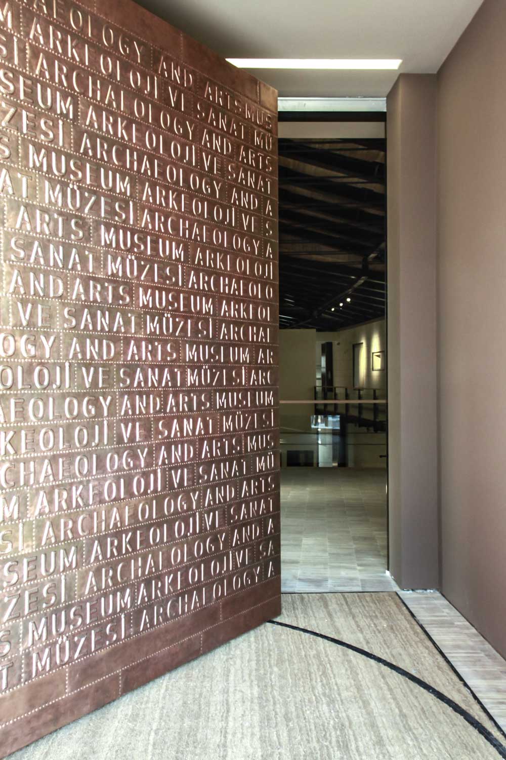 Decorative museum branding on a wall reading: Archaeology and Arts Museum / Arkeoloji ve Sanat Müzesi in the entryway of gallery spaces.