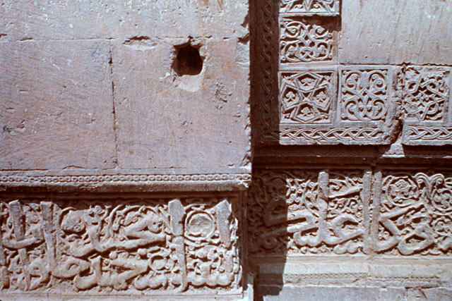 Detail view of the gate showing Quranic inscription on an arabesque background