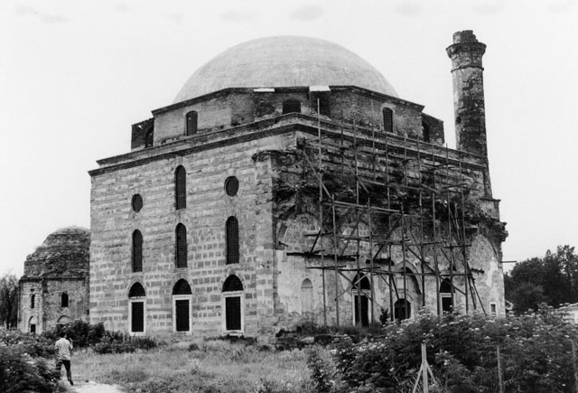 Exterior view from north showing mosque with collapsed portico and minaret; the mausoleum with its damaged dome is seen behind