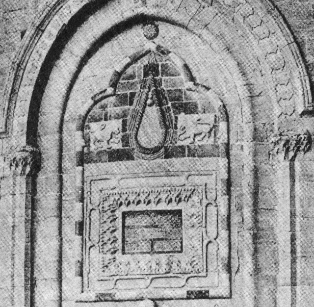Detail of portal on entry tower showing framed inscription above doorway, with tear motif flanked by lion figures above