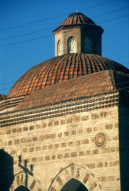 Nilüfer Hatun Imareti - Exterior detail from southern wall of portico showing decorative disk and the tiled dome and lantern of the central hall