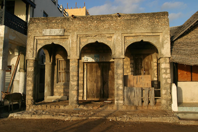 Street view of concrete block colonnaded entrance portico with coral rag entablature