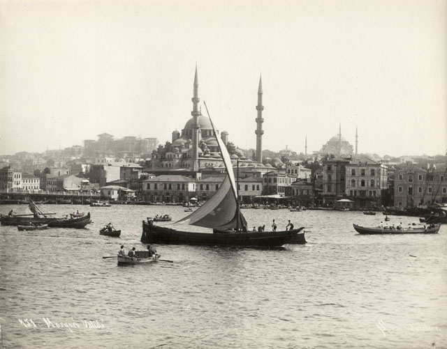 Yeni Camii Külliyesi - Exterior view from Golden Horn looking south, with the Galata Bridge seen in the left foreground. In the background are the Nuruosmaniye Mosque (right) and the Ottoman Public Debt Administration building (Düyun-i Umumiye, left), seen under construction