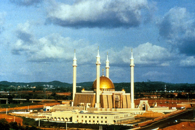 Exterior view showing gold dome, corner minarets and sloped façade