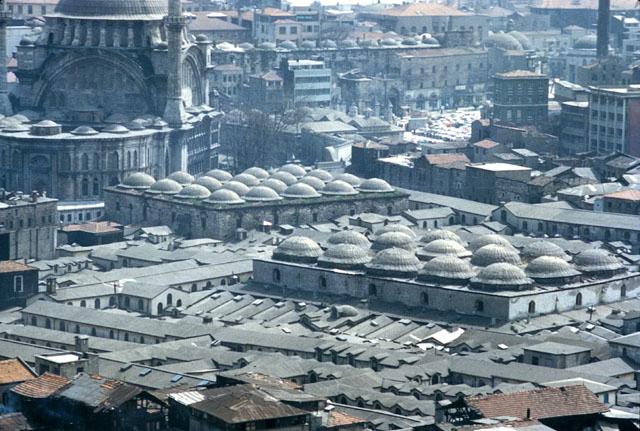 Elevated view from west showing the domes of the Old Bedesten (right) and the Sandal Bedesten (left) among the roofs of the bazaar , and the Nuruosmaniye mosque with its oval courtyard