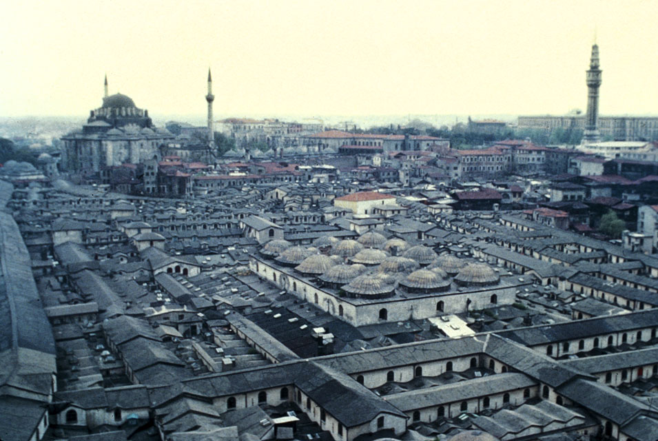 General view looking west from a minaret of the Nuruosmaniye Mosque with the Old Bedesten at the center, the tall gable roof of the Kalpakçilar Street frames the photograph on the right.  The Bayezid Mosque is seen in the left background, and Bayezid Fire Tower appears in front of the Istanbul University building on the right