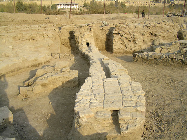 Excavated brick channel at the base of the central axis, with footings of stone wall and gateway behind