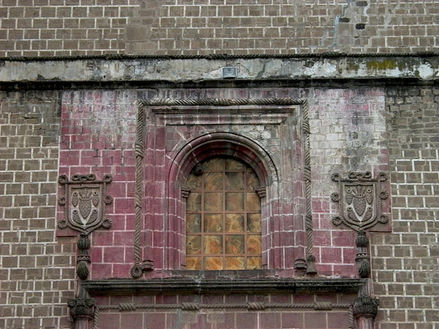 Exterior detail view of arched window, flanked with the Franciscan emblem (the five stigmata), above portal (Portada)