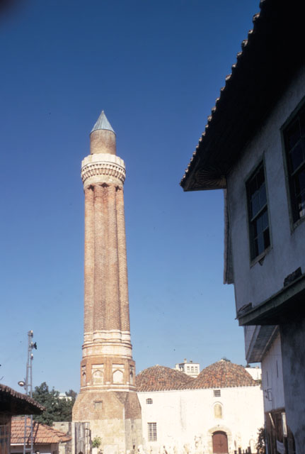 Exterior view of mosque and minaret, with wooden house in foreground