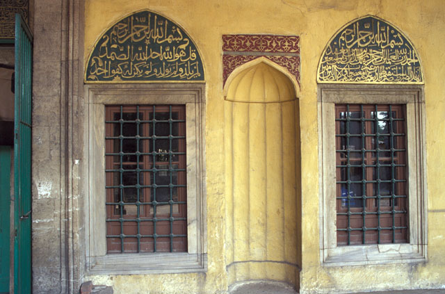 Two windows and a mihrab niche to the right of the main portal, the tympana are adorned with the Koranic verses of Felak and Nas written in high relief with gold letters