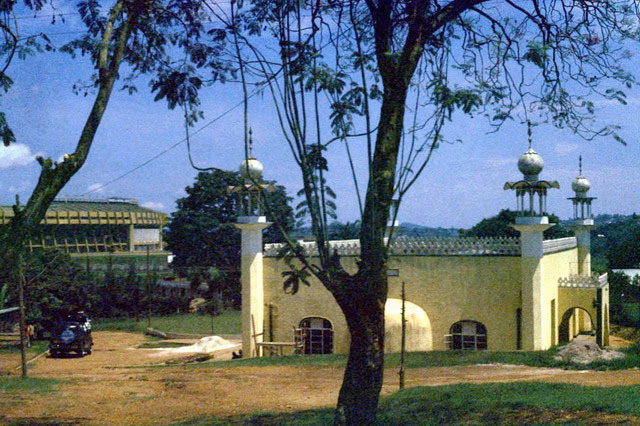 Exterior view from main road, showing qibla wall with mihrab apse, with Mandela National Stadium seen in the background
