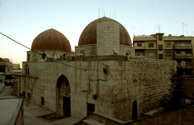Exterior view showing both domes and collage of building materials from different periods; the minaret is seen under construction