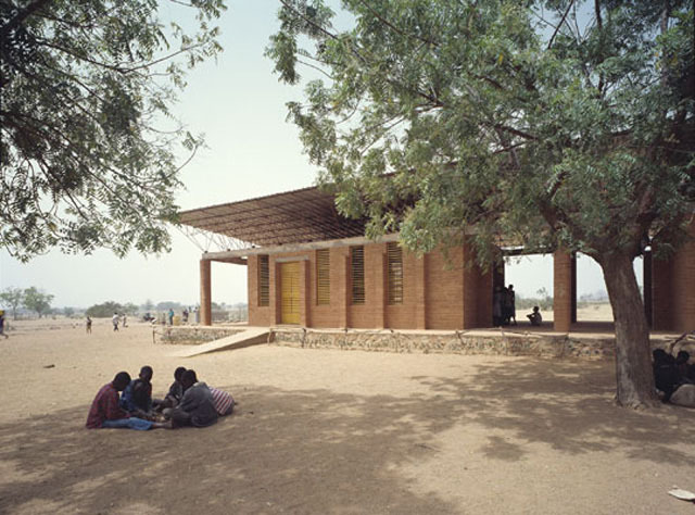 Partial exterior view from south, showing western classroom, with children gathered under trees in the foreground