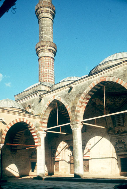 Exterior view of the eastern corner of courtyard, showing vaulted bay from original portico and the minaret with double balcony rising from behind it