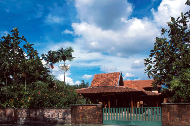Entrance gate to the house complex; the steeped roof form of the entrance pendopo pavilion can be seen