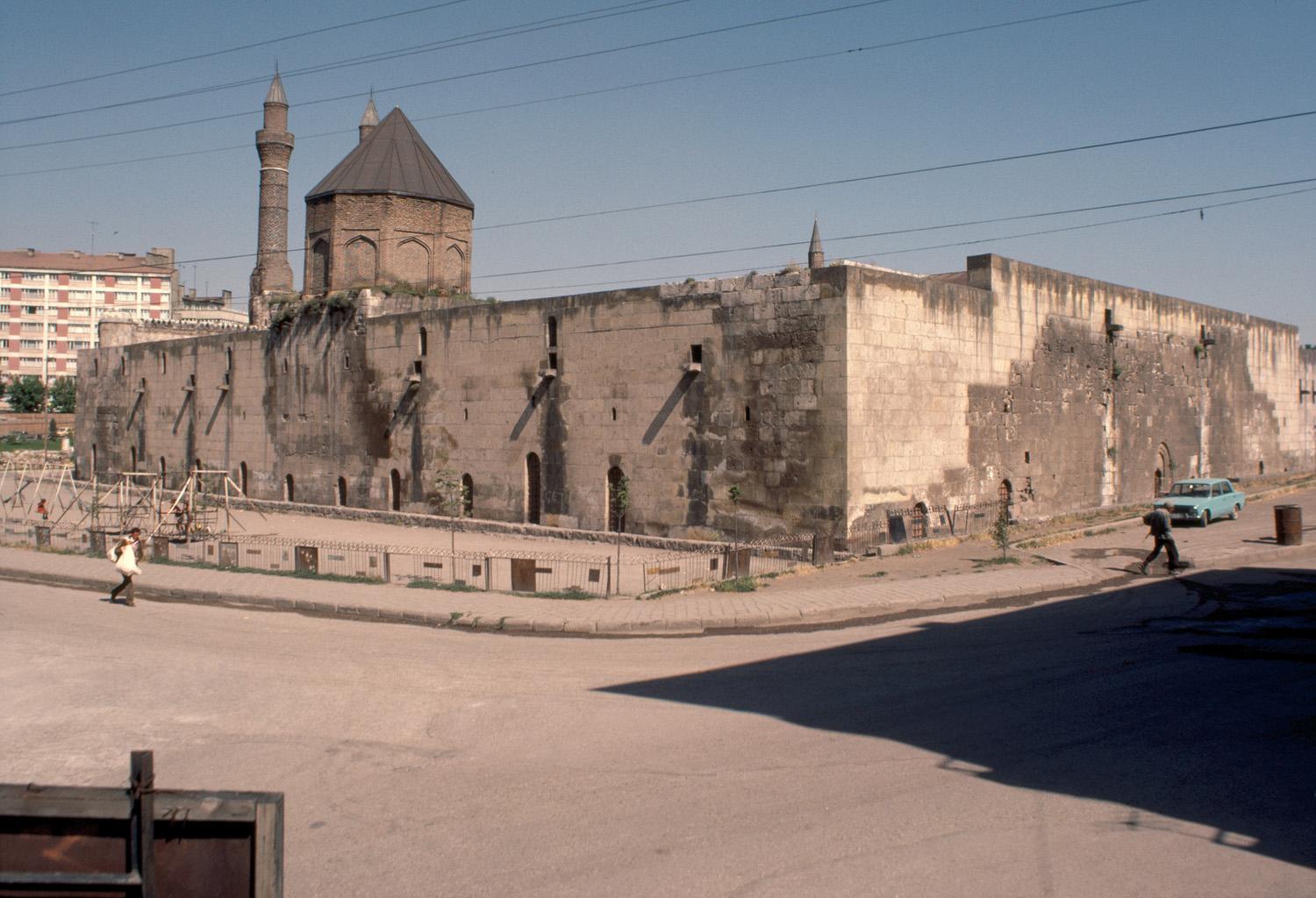 Exterior view from southeast, looking at the southern elevation with the tomb tower; the twin minarets of Çifte Minaret Madrasa are seen beyond.