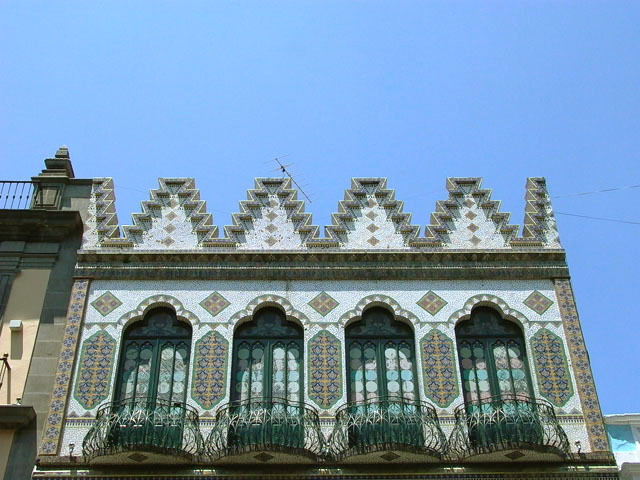Exterior view of top-most level showing four trefoil arched openings to individual balconies and zigzag merlons above