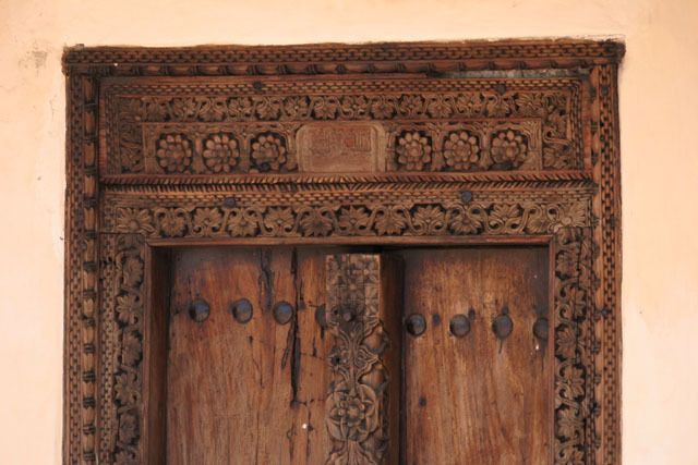 Detail view of Swahili door showing header with rosette carvings and center-post with foliated carvings