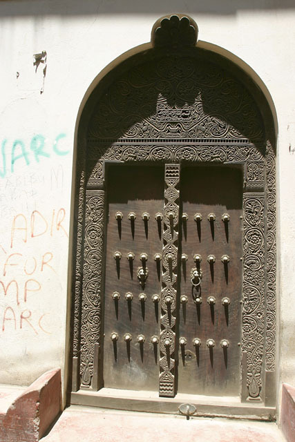 Exterior view of Swahili door with arched lintel, brass studded detailing and frankincense tree decorative detailing