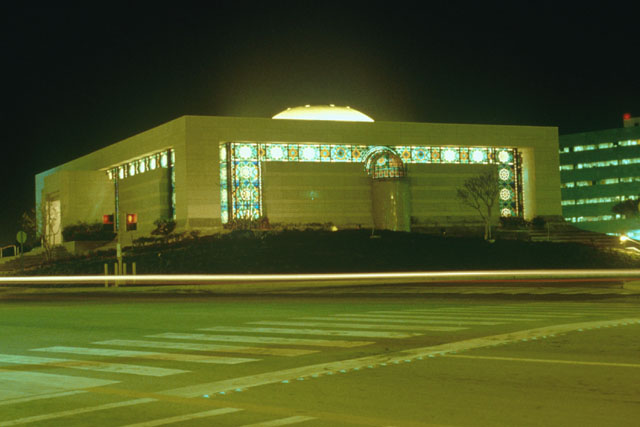 Exterior view of façade taken at night, showing elaborate colored glass frame