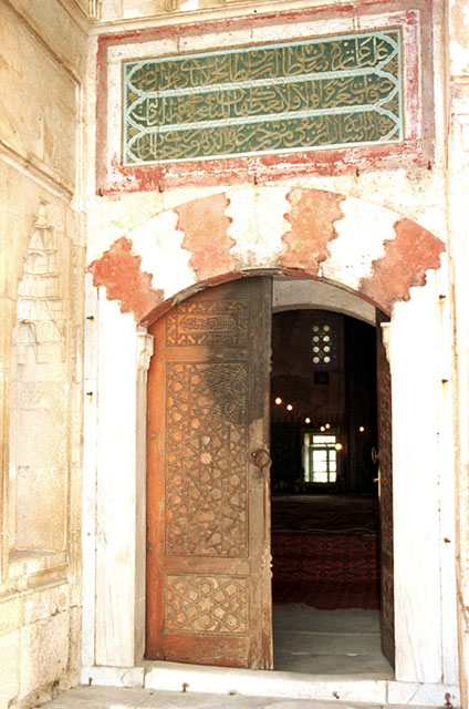 Exterior detail showing carved wooden door and inscriptive plaque in Arabic giving name of donor and date of completion