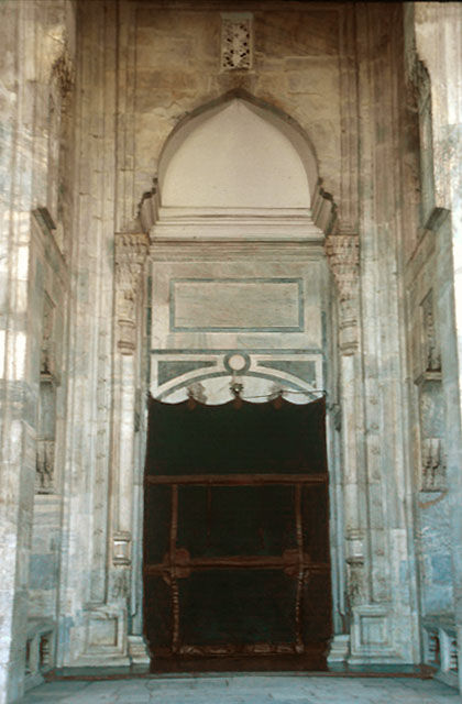 The entrance to the mosque framed at top with an ogee arch resting on two circular columns with protruding capitals.  Seats are carved into the walls on both sides of the recessed entrance