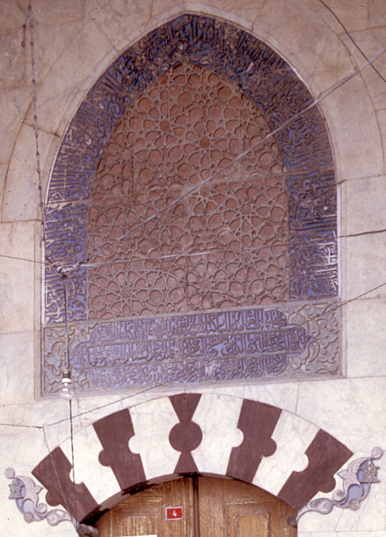 Detail from mosque portal showing interlocked stars decorating tympanum, bordered by carved inscriptions.  The red and white voussoirs of the entry arch, seen below, are cut into unique shapes
