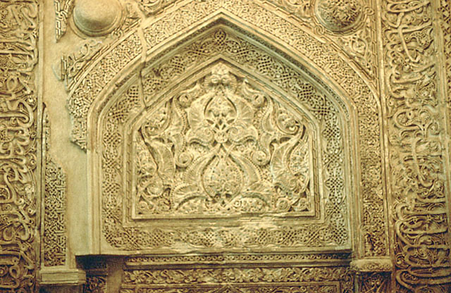 Detail of mihrab showing floral stucco decoration and inscriptions in upper hood
