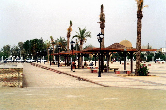 Metal and wood shelters and flower beds in public square, with the library and mausoleum seen in the background