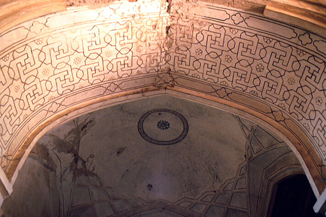 Interior detail of ceiling of arch and dome in the background. Arch has geometric patterns.