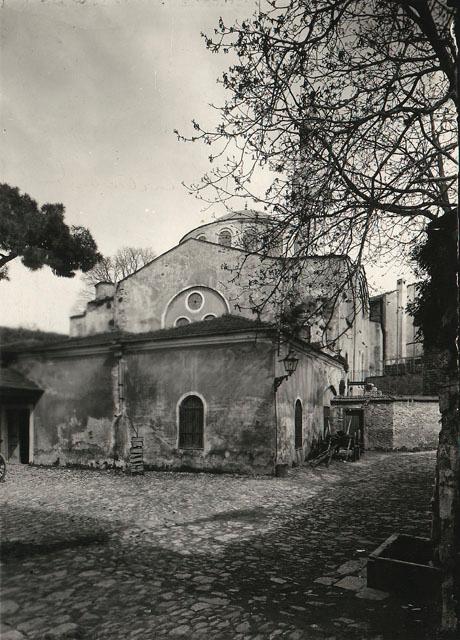 Exterior view from west-southwest, showing inner and outer narthex covered by a single sloping dome, with the domed nave rising from behind.  A small addition that no longer exists is seen to the right of the narthexes in this early photograph, in addition to the original minaret, which is partially obscured by a tree