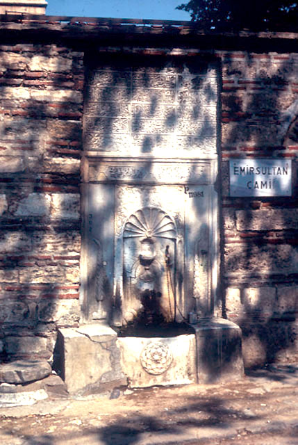 View of historic fountain (b.1743) in wall next to kibla wall of mosque; the inscription is a poem praising the soul of Emir Sultan