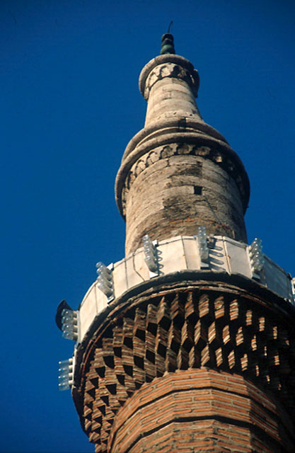 Detail from minaret, showing saw-toothed projection of the brick serefe and the carved stonework of the spire