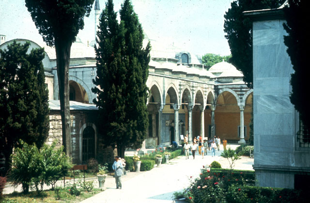 The Ağalar Mosque - View past the corner of the Library of Ahmed III (right) and the Mosque of the Aghas (left) in the Third Court: looking towards the arcade before the nineteenth century Dormitory of the Privy Chamber Pages <i>(Has Odalilar Kogusu)</i> and the Pavilion of the Blessed Mantle <i>(Hirka-i Serif Dairesi)</i>, formerly the Sultan's Apartments <i>(Has Odasi)</i>
