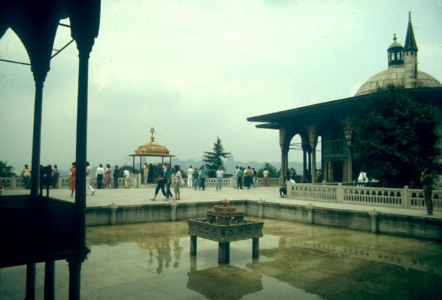 View looking north from the colonnade of the Pavilion of the Blessed Mantle towards the Terrace of Ibrahim I (1640-48) that overlooks the Bosphorus. The gilded Sundown Bower (Iftariye Köskü) is seen at the center of the terrace with the Baghdad Kiosk on its right. The balcony of Süleyman I projects over the pool on the left