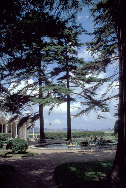 View of harem gardens looking north, showing small pool among pine trees and the sea kiosk (Yali Köskü), seen partially on the left.  The European coast of Istanbul appears in silhouette behind the seawall