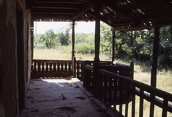 <p>This view within he upper level porch (pridvor) reveals the extended sitting area (cerdac or foişor) that overhangs the stairway. The simple framework, shaped to articulate the narrow gallery columns, and notched railing planks give this area an interesting visual fabric. The widely spaced balustrades along the walkway are in contrast to the patterned notching of the end rail panels and the different notching of rail panels and corner posts that define the sitting area. This porch space would typically overlook the yard of the gospodărie, or homestead.</p>